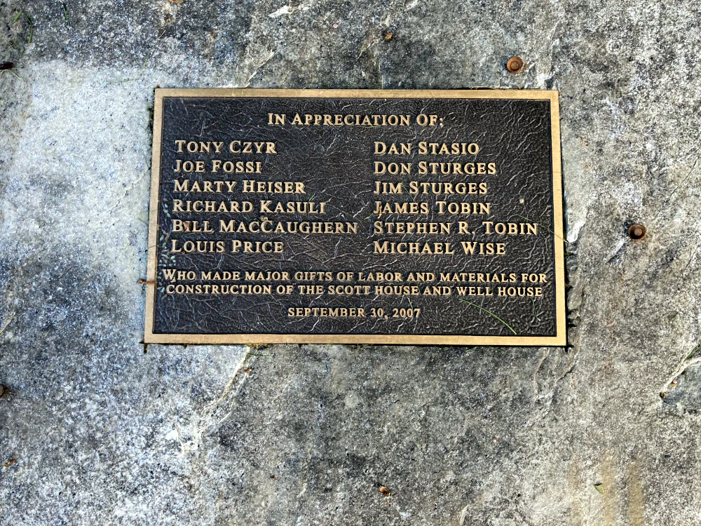 A bronze plaque set into stone; the plaque reads: "In appreciation of Tony Czyr, Joe Fossi, Marty Heiser, Richard Kasuli, Bill MacCaughern, Louis Price, Dan Stasio, Don Sturges, Jim Sturges, James Tobin, Stephen R. Tobin, and Michael Wise who made major gifts of labor and materials for construction of the Scott House and Well House, September 30, 2007.